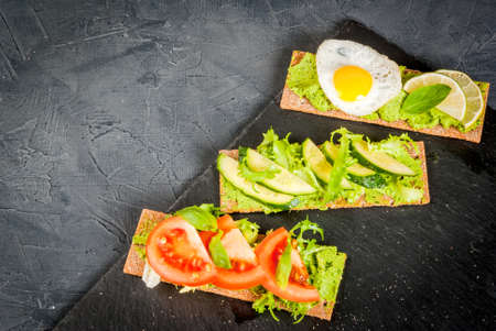 Healthy Eating, Diet sandwiches on gluten-free loaves - with guacamole, fresh vegetables (tomato, cucumber), egg, lime, lettuce and basil, On a stone (concrete) gray table, top view, copy spaceの写真素材