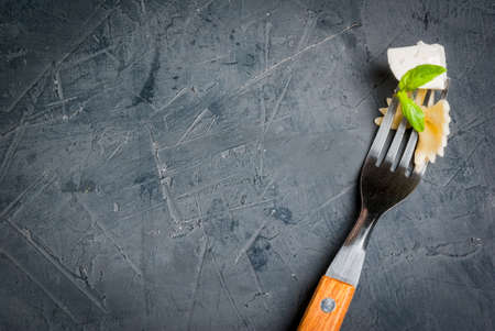 Fork with pasta farfalle, cheese and basil on the kitchen gray stone table