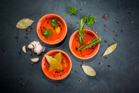 Selection of scented oils from herbs and spices: rosemary, garlic, pepper, parsley, bay leaf. On a...