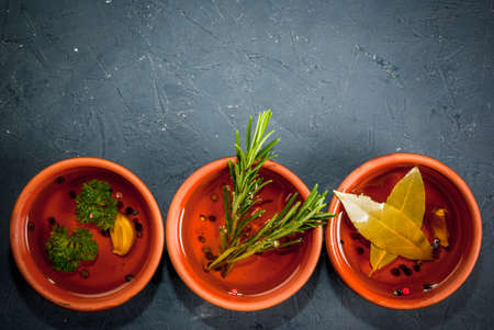 Selection of scented oils from herbs and spices: rosemary, garlic, pepper, parsley, bay leaf. On a dark gray stone kitchen table. Top view, copy spaceの写真素材