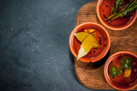 Selection of scented oils from herbs and spices: rosemary, garlic, pepper, parsley, bay leaf. On a cutting board, on a dark gray stone kitchen table. Top view, copy spaceの写真素材