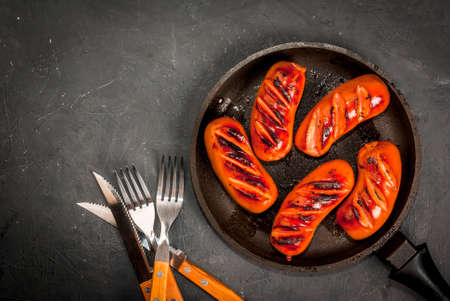 Grilled sausages, homemade, in a pan, on a concrete gray stone table, top view. With ketchup and spices (pepper), copy spaceの写真素材