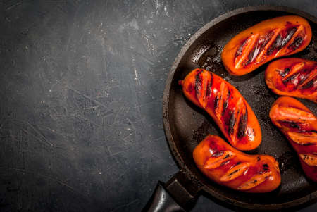 Grilled sausages, homemade, in a pan, on a concrete gray stone table, top view. With ketchup and spices (pepper), copy spaceの写真素材
