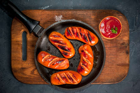 Grilled sausages, homemade, on a cutting board on a concrete grey stone table, top view. With ketchup and spices (pepper)の写真素材