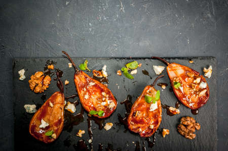 Fresh summer salad - grilled pears, cheese with blue mold with walnuts and caramel sauce. On the black slate platter. Top view, copy spaceの写真素材