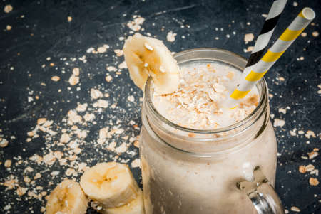 Smoothies with yogurt, banana and oatmeal in a mason jar. On a dark gray concrete stone background, with ingredients for cooking. Copy space, close viewの写真素材