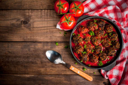 Homemade meatballs from minced beef in tomato sauce with fresh herbs in a frying pan on a wooden table. top view, copy spaceの写真素材