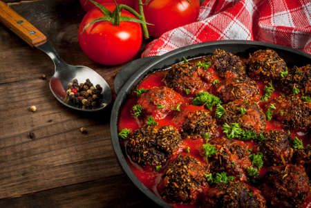 Homemade meatballs from minced beef in tomato sauce with fresh herbs in a frying pan on a wooden table. close view, copy spaceの写真素材