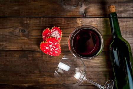 Bottle of wine and two glasses - one empty, one full poured, biscuits valentines in the form of hearts with red icing, on a wooden table, top view copy spaceの写真素材