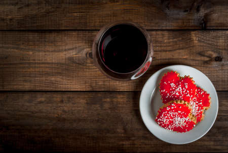 Background for Valentine's Day: glass with wine and three biscuits in shape of hearts with red icing, top view, copy spaceの写真素材