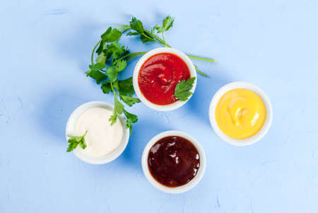 Classic set of sauces in white saucers: American yellow mustard, ketchup, barbecue sauce,...