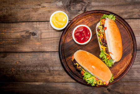 Homemade hot dogs with sausages, fresh lettuce, cucumbers, herbs, mustard and ketchup. On wooden table close view, copy spaceの写真素材