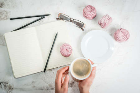 Home spring vacation, relax, work. White stone concrete desk with notepads, coffee and pink berry pastries (marshmallows). The girl holds a cup in his hands top view copy spaceの写真素材