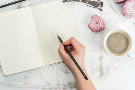 Home spring vacation, relax, work. White stone concrete desk with notepads, coffee and pink berry pastries (marshmallows). The girl wrote in pencil in a notebookの写真素材