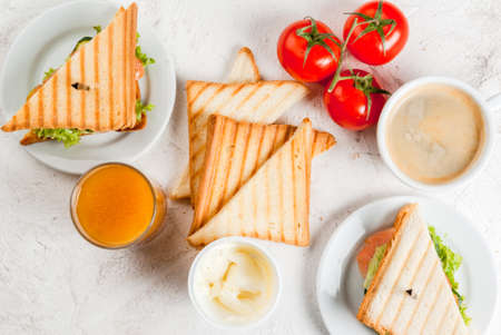 Breakfast with club sandwiches with fresh tomatoes, lettuce and cucumbers, salmon (trout), coffee and freshly squeezed juice, on white stone concrete table top viewの写真素材
