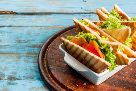 Club sandwiches with fresh lettuce, tomato, cucumber and salmon (trout). On crunchy toast. On blue rustic table, picnic, copy spaceの写真素材