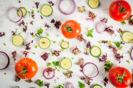 Spring salad concept: fresh lettuce, onion rings, parsley, greens, cucumbers and tomatoes on a white table. Flat top view, background with ingredientsの写真素材