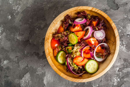 Salad of fresh spring vegetables and lettuce leaves in a wooden bowl on a concrete stone gray table, top view, copy spaceの写真素材
