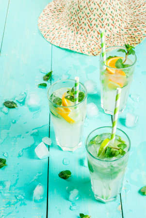 Selection of summer refreshing cocktails with mint (lemonade or mojito): with lemon, orange, lime. On light blue wooden table, bright sunlight. Copy space, close viewの写真素材