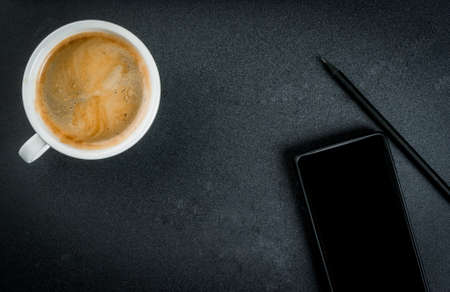 Smartphone and a cup of coffee on the office black table, top view, copy spaceの写真素材