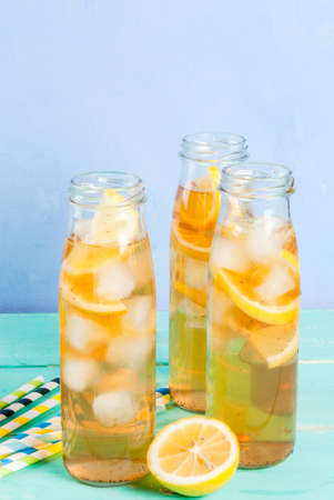 Iced summer drink - tea with lemon on a blue wooden table, in bottles with striped straws copy spaceの写真素材