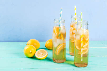 Iced summer drink - tea with lemon on a blue wooden table, in bottles with striped straws copy spaceの写真素材
