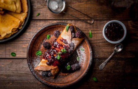 Delicious homemade breakfast: french crepes with forest fruit, topped with jam and filled with...