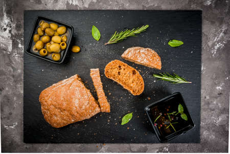 Italian food, snack: dark rye ciabatta with basil, rosemary, fragrant oil and green olives. On the...