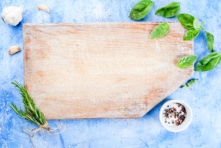 Food background: a cutting board on a light blue stone concrete table with spices and herbs for cooking - garlic, rosemary, basil, salt, pepper. Italian styleの写真素材