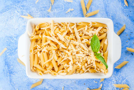Macaroni with grated cheese in a pot ready to bake. On a light blue stone concrete table top view copy spaceの写真素材