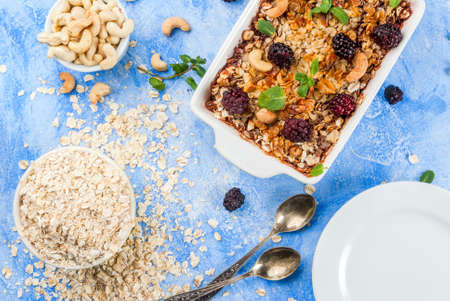 Freshly baked diet berry crumble with oatmeal with fresh berries blackberries decorated with mint leaves. In a frying pan for baking, with ingredients on blue stone concrete table, top view copy spaceの写真素材