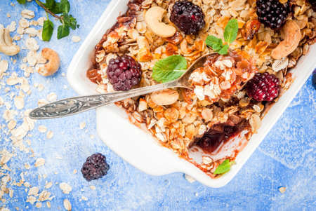 Freshly baked diet berry crumble with oatmeal with fresh berries blackberries decorated with mint leaves. In a frying pan for baking, with ingredients on blue stone concrete table, top view copy spaceの写真素材