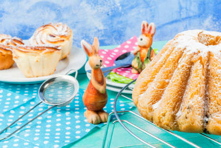 Beautiful Easter ring cake and small Easter cupcakes decorated with icing sugar, on a decorated festive spring table with toy bunnies and sheepの写真素材