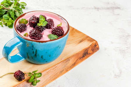Milkshake or frozen berry yogurt in a cup, with berries fresh blackberries and mint leaves. On the white stone concrete table, copy spaceの写真素材