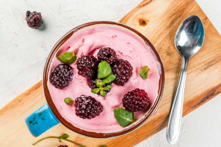 Milkshake or frozen berry yogurt in a cup, with berries fresh blackberries and mint leaves. On the white stone concrete table, copy spaceの写真素材