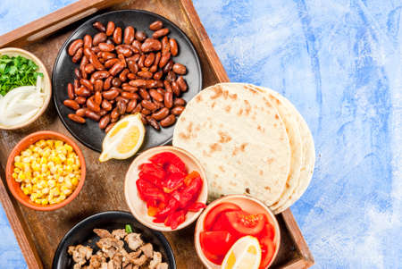 Ingredients for Mexican food on a tray: beans, stew beef, corn, tomatoes, red pepper, onion, herbs, tortillas taco, top view copy spaceの写真素材