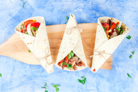 Street fast Mexican food, freshly prepared, homemade sandwiches burrito with beans, beef, corn, peppers, tomatoes and herbs. On the blue background of the concrete stone, top view copy spaceの写真素材