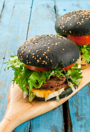 Freshly homemade black burgers with cheese, beef minced steak, tomato and lettuce. Summer sunny, old light blue rustic table, copy spaceの写真素材
