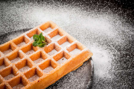 Freshly baked Belgian waffles, sprinkled with powdered sugar. On a black plate on a black stone table. Close view, copy spaceの写真素材