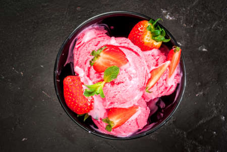 Strawberry ice cream pink with strawberries and mint. In a small bowl, on the black concrete table, copy space top viewの写真素材