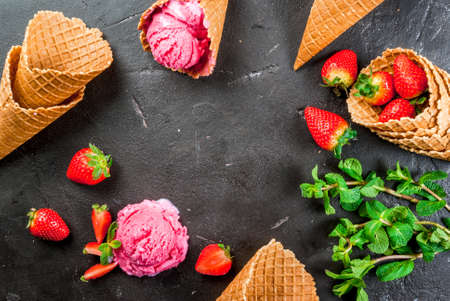 Pink strawberry ice cream. In a small bowl, on the black concrete table with ice cream cones, a bunch of mint and strawberries, top view, copy space, frameの写真素材