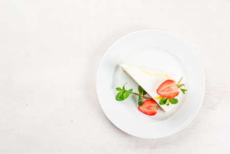 Light dessert: classic cheesecake, decorated with mint and strawberries. On a white plate, on a...