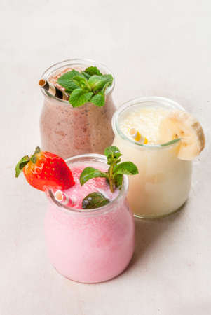 Selection of classic milkshakes in small jars: chocolate, strawberry, banana. On a white wooden table, with tubes, copy spaceの写真素材
