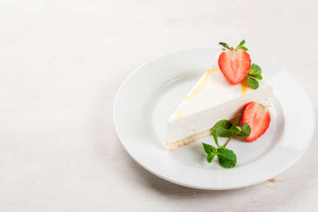 Light dessert: classic cheesecake, decorated with mint and strawberries. On a white plate, on a white wooden table. Close view copy spaceの写真素材