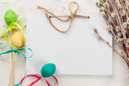 Funny children's food for Easter, decoration. Candy pop cakes on a stick, with multi-colored ribbons, willow twigs and a notepad for congratulations. On a white table, top view, holiday background, copy spaceの写真素材