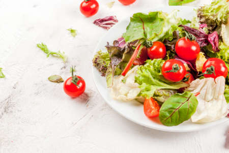 Light salad of green leaves and tomatoes. On a white concrete table, With ingredients, copy spaceの写真素材
