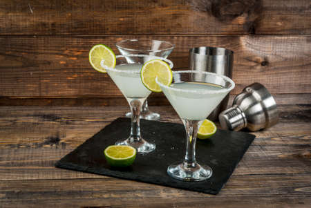 Alcohol cocktail margarita, martini or gin tonic with lime. On a wooden table on the slate board, with lime and shaker, copy spaceの写真素材