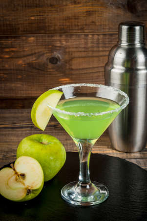Alcoholic cocktail - Appletini. martini, margarita with apple. Decorated with slice of green apple, with a shaker on a black slate on a wooden table, copy space, verticalの写真素材