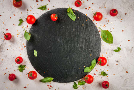 Preparation of food background: fresh tomatoes, basil leaves, parsley and seasoning, on white concrete table, top view, with slate cutting boardの写真素材