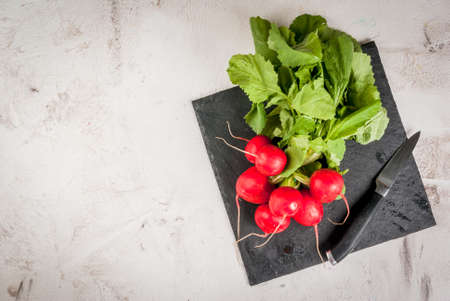 Bunch of fresh radishes on a white concrete table, on a slate board with a knife, top view, copy spaceの写真素材